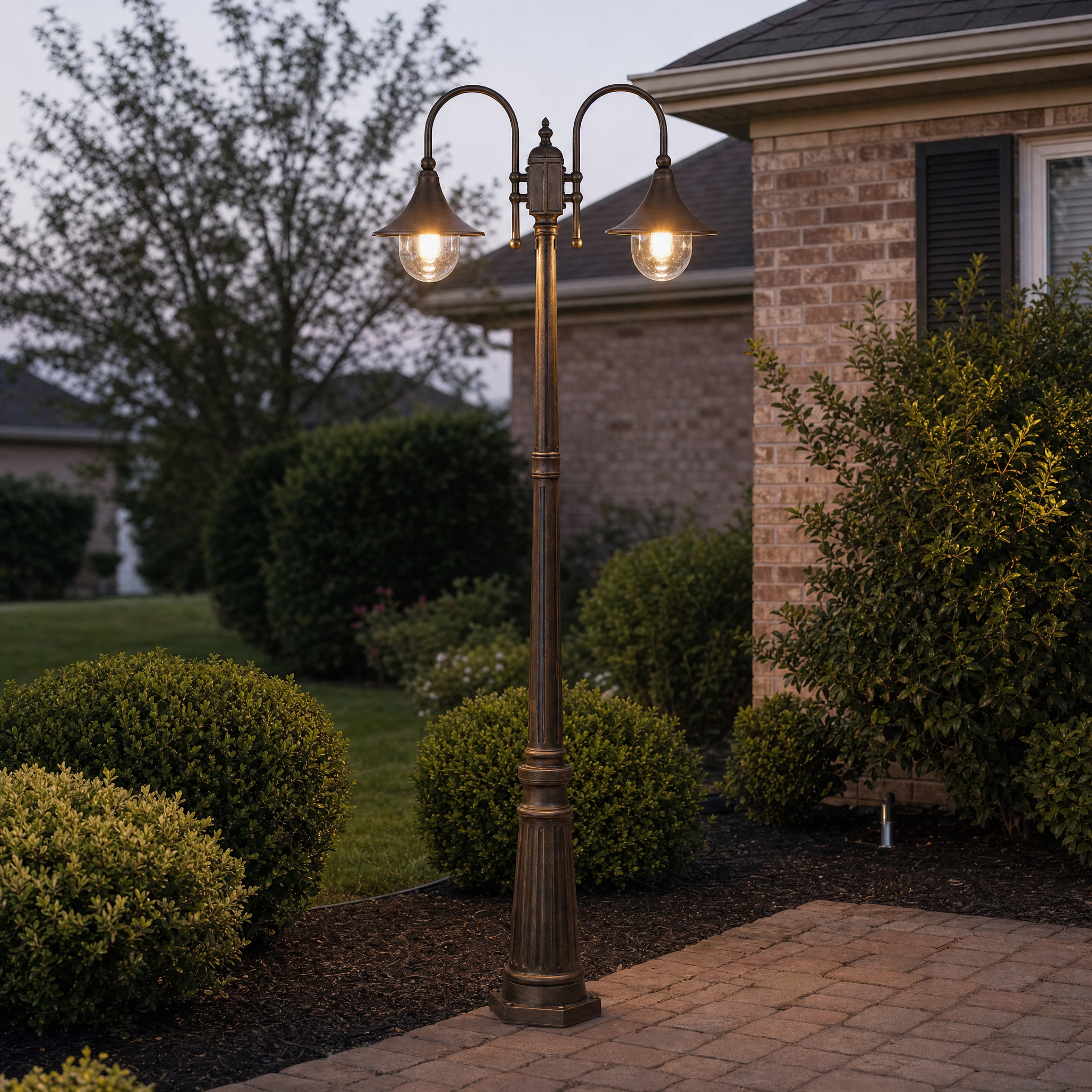 Vintage double-head flared pathway pole light glowing on a paver walkway at dusk