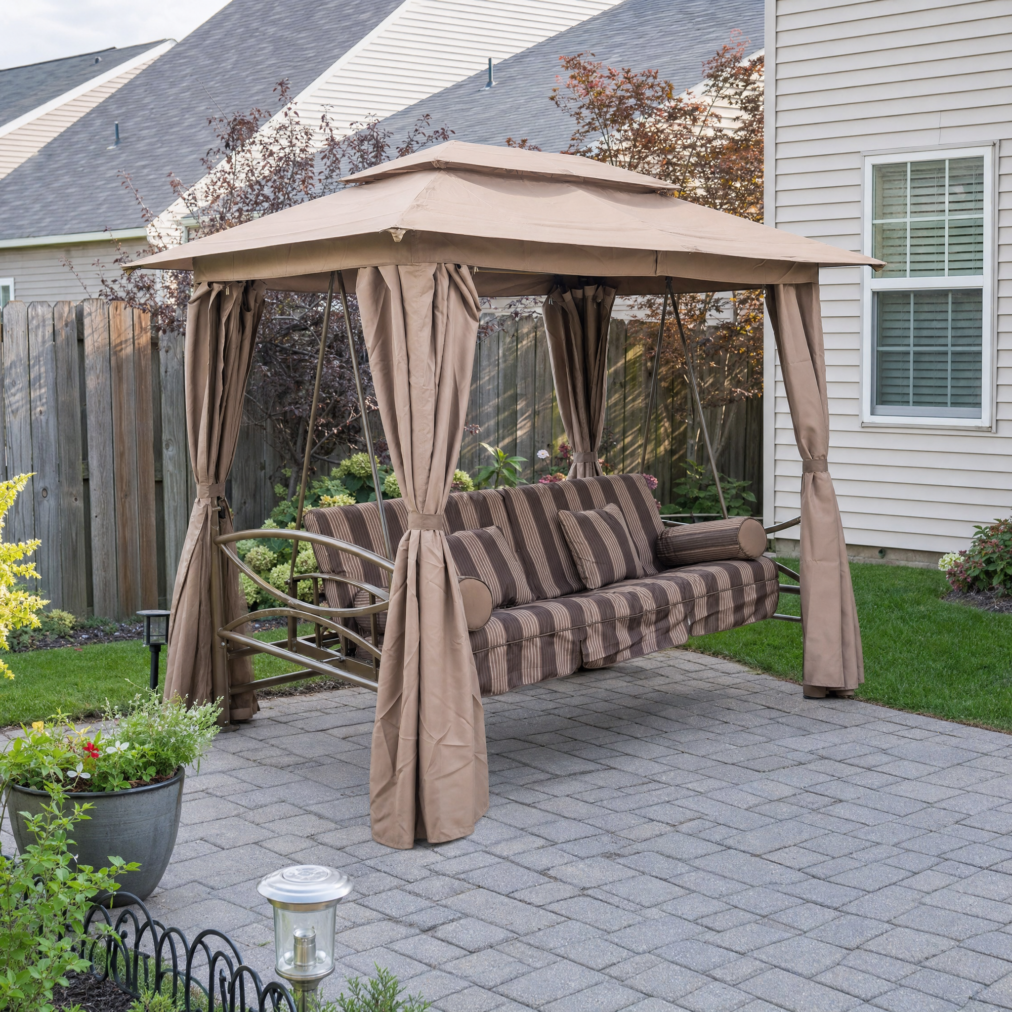 3-person swing glider with tan peaked canopy and brown striped cushions on patio