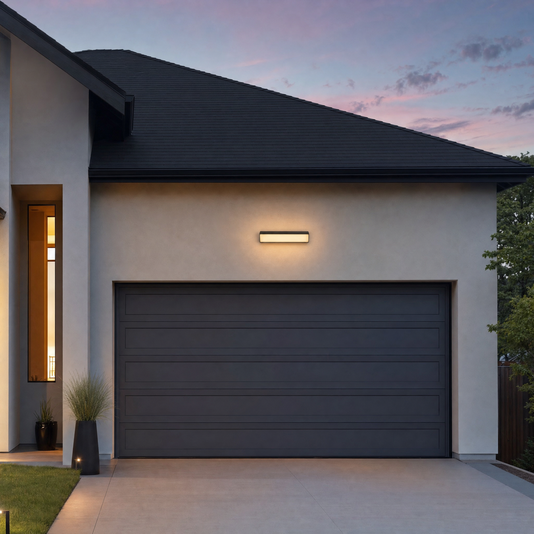 Horizontal black LED bar wall light mounted above a modern home garage at dusk