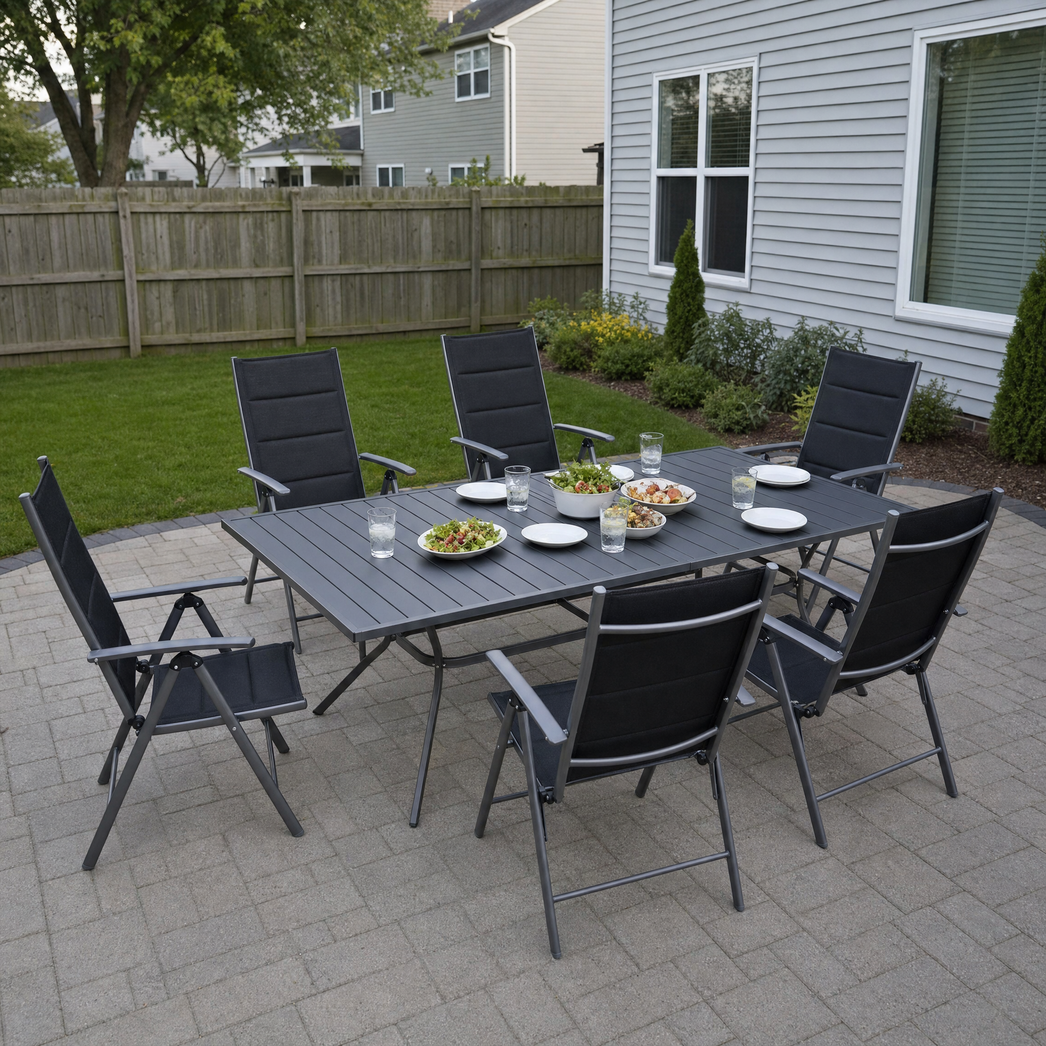 Dark-grey slat dining table with six black folding recliner chairs on patio